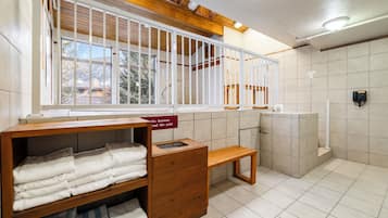 A hotel bathroom with a wooden bench, a towel rack, and a sign indicating no footwear beyond a certain point.