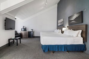 A hotel room with a large bed, a desk, a coffee machine, and a flat-screen TV. - Red Carpet Inn (Banff)