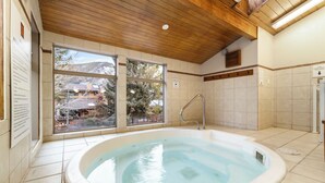 A hot tub in a room with large windows, wooden ceiling, and tiled walls.