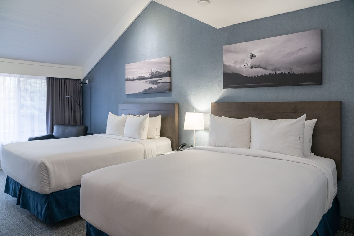 Habitación de hotel con dos camas, un ventanal con cortinas y dos cuadros colgados en la pared.