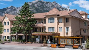 A hotel with a mountain backdrop, featuring a covered outdoor seating area and a stone facade. - Red Carpet Inn (Banff)