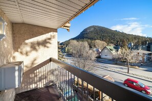 A balcony with a view of a street, a mountain, and a red car passing by.