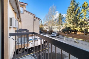 A residential street with a parked truck and a car, a building with a balcony, and a row of evergreen trees. - Red Carpet Inn (Banff)