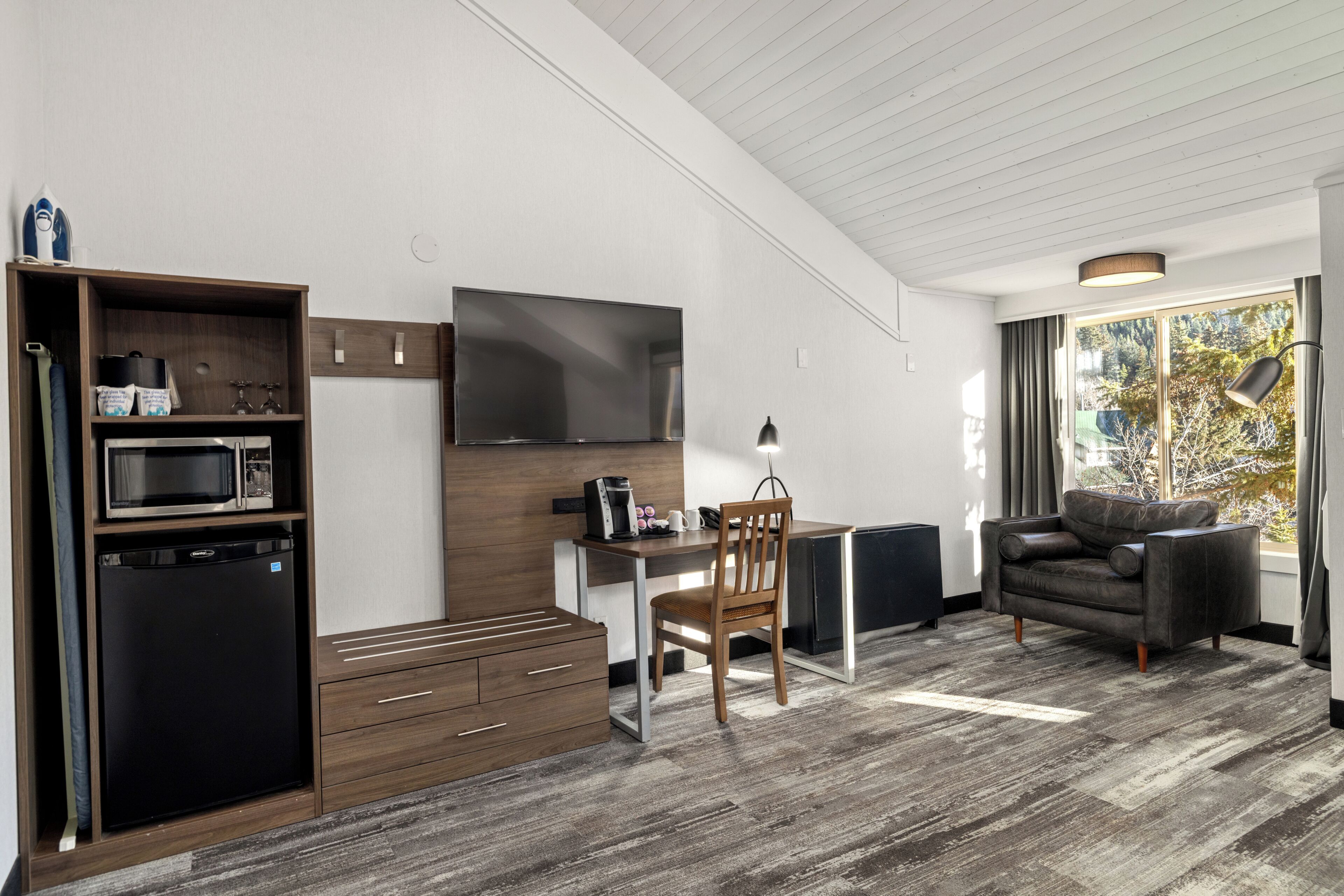Un espace de vie compact comprenant un coin cuisine, un téléviseur à écran plat, un coin repas et un espace salon avec vue sur l’extérieur.