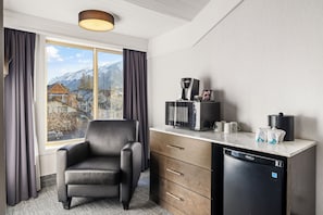 A hotel room with a view of snow-capped mountains, a black leather chair, a coffee maker, a microwave, and a dishwasher. - Red Carpet Inn (Banff)