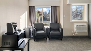 Habitación de hotel con escritorio, dos sillones, televisor y ventana con vista a árboles y montañas.