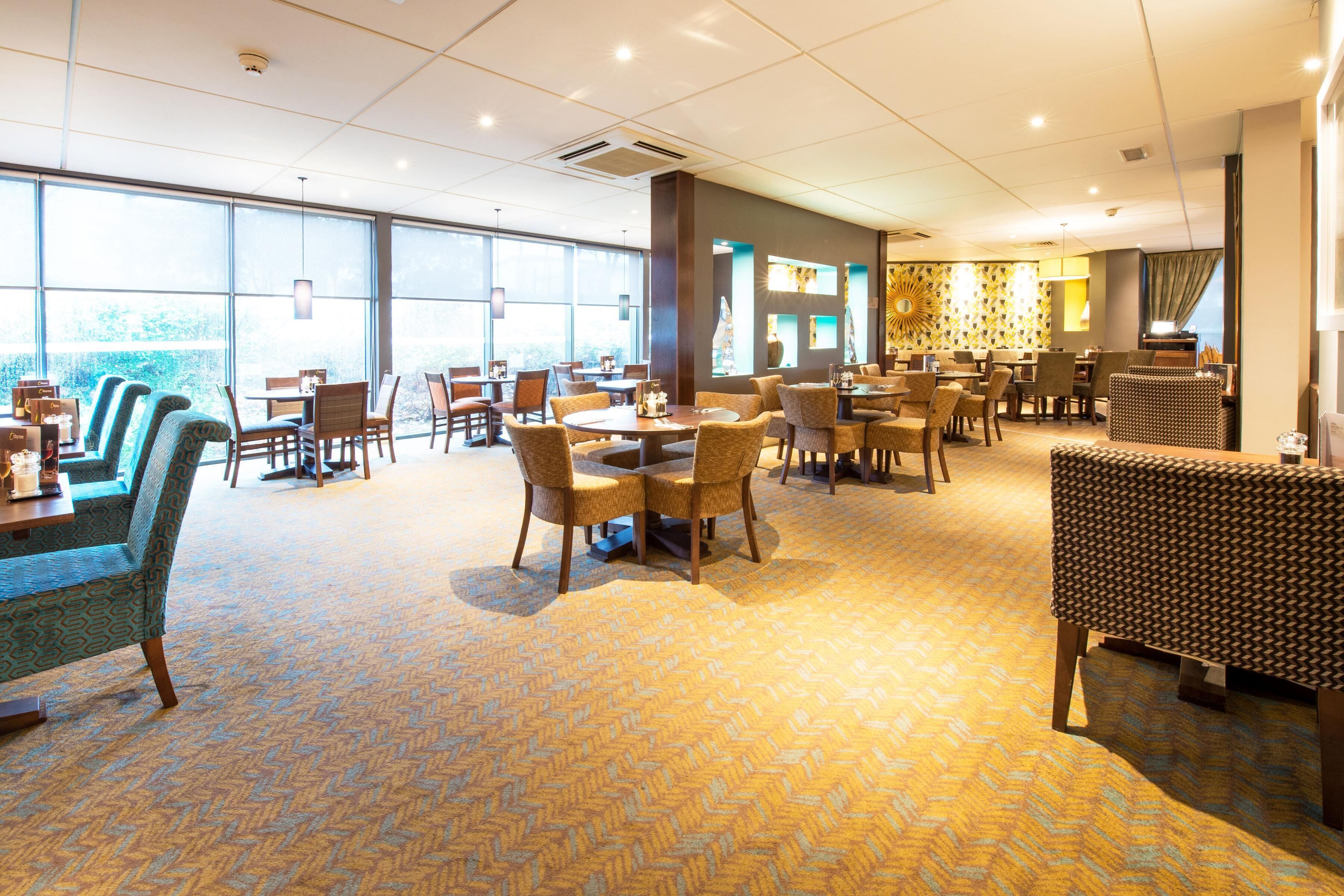 A spacious dining area with multiple tables and chairs, large windows, and a patterned carpet.