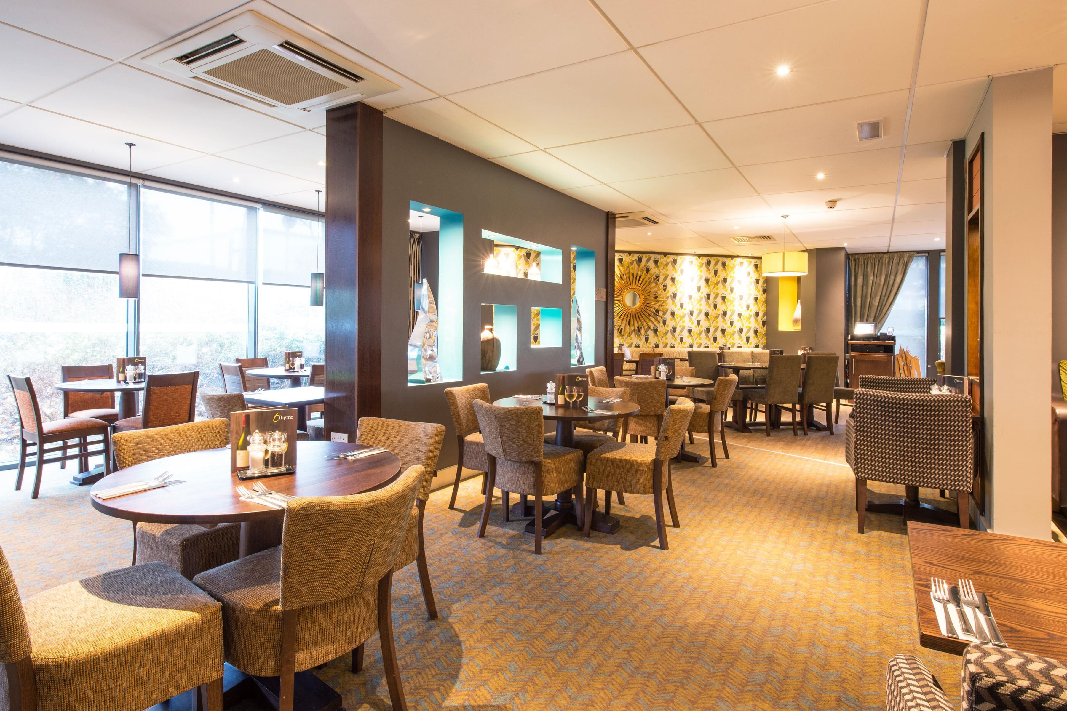 A hotel lobby with multiple dining areas, large windows, and a patterned carpet.