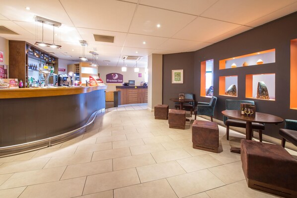 A hotel lobby with a curved reception desk, seating area with tables and chairs, and a wall with framed artwork.
