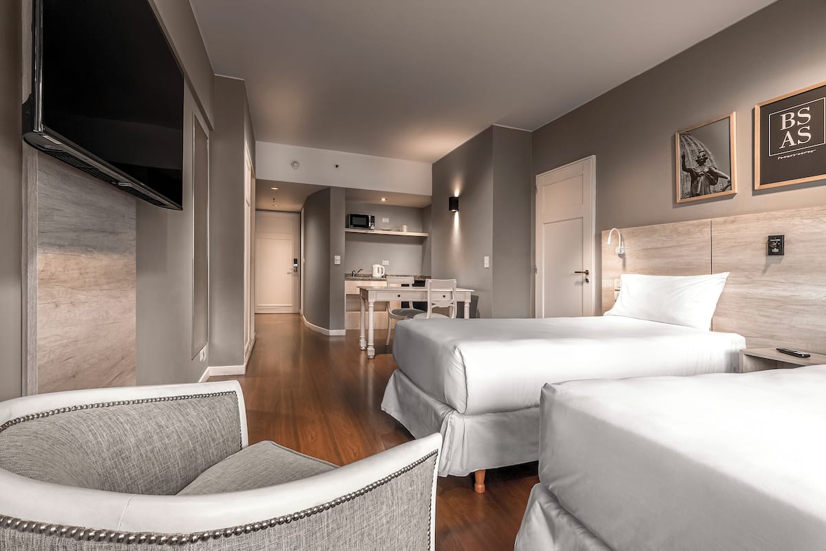 A hotel room with two beds, a TV, a desk with a chair, and a microwave.