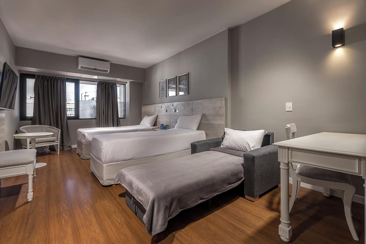 A hotel room with two beds, a desk, a chair, a small table, and a window with curtains.