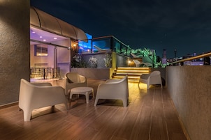 Uma área de estar moderna ao ar livre, com cadeiras contemporâneas e guarda-corpo de vidro com vista para a paisagem urbana.