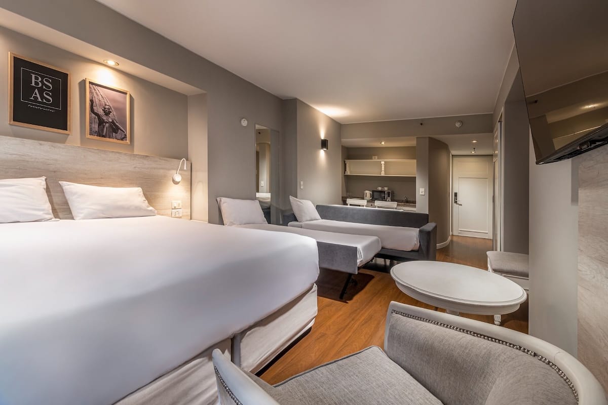 A hotel room with two beds, a sitting area, a small table, and a kitchenette.
