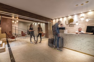 Uma área de recepção moderna com balcão de mármore, uma tela digital e uma placa com a inscrição 'AMÉRICA PLAZA'.