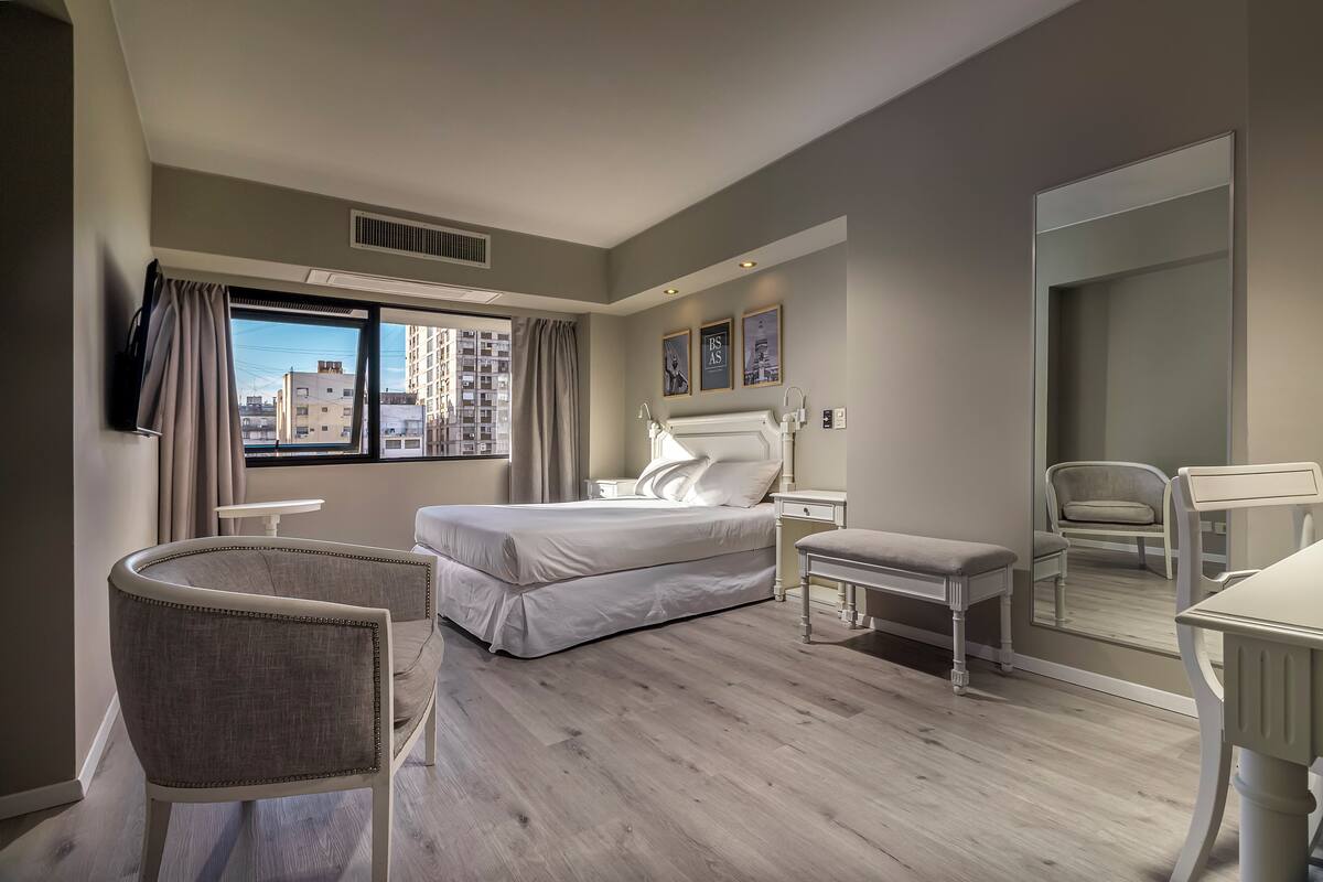 A modern hotel room with a large bed, a desk, a chair, and a view of the city.