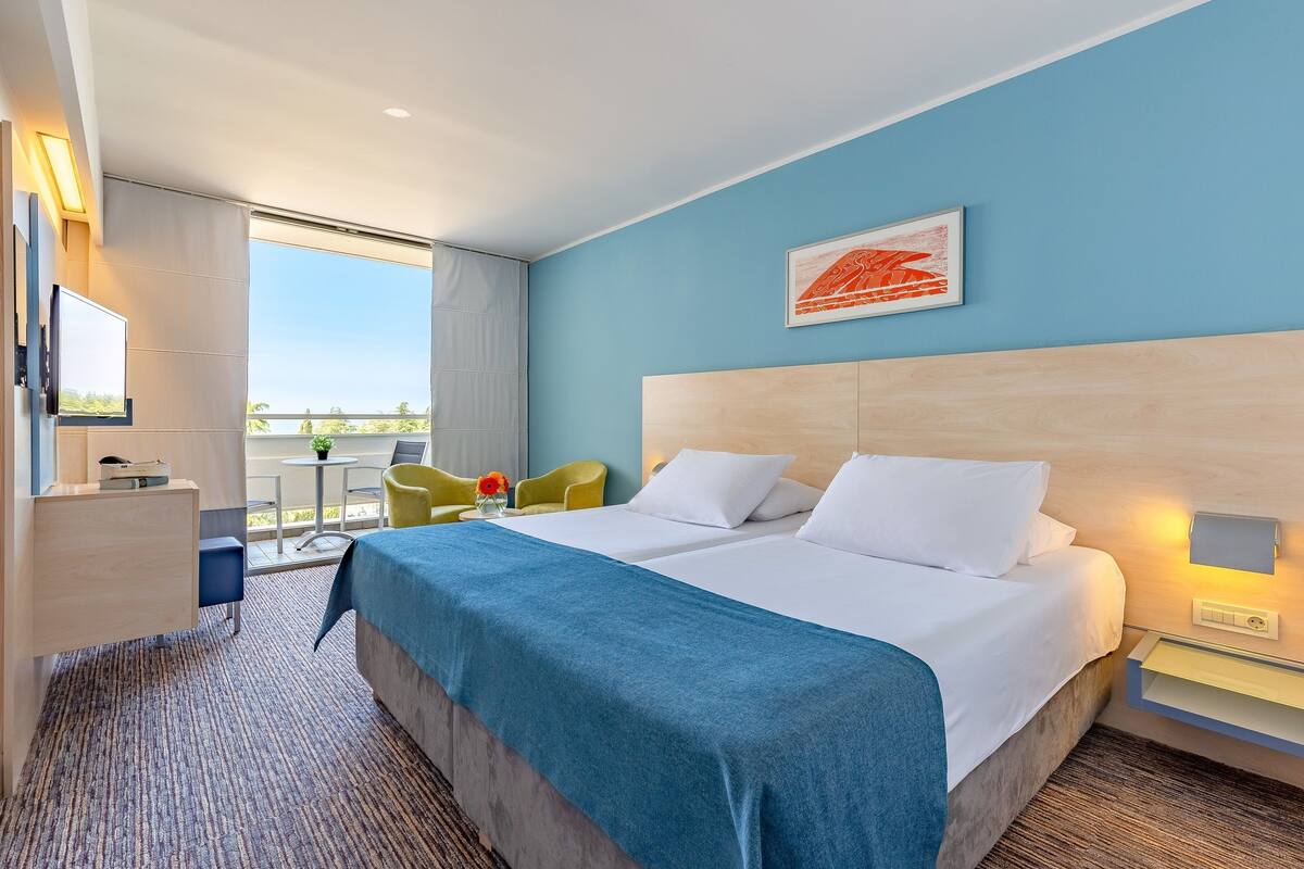 Habitación de hotel con una cama grande, un escritorio, una silla y vistas al exterior.