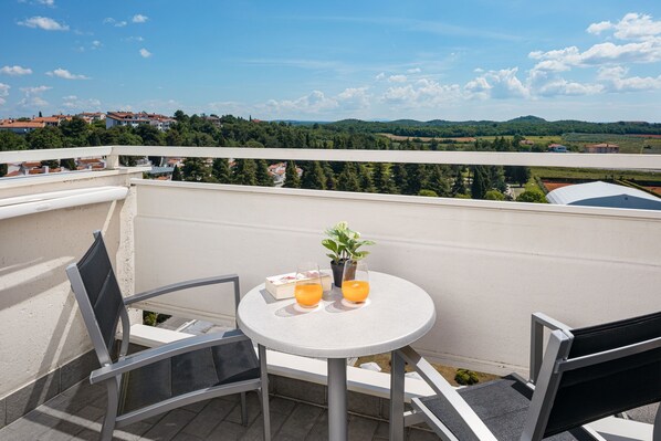 A balcony with a round table, two chairs, a potted plant, and two glasses of orange juice.