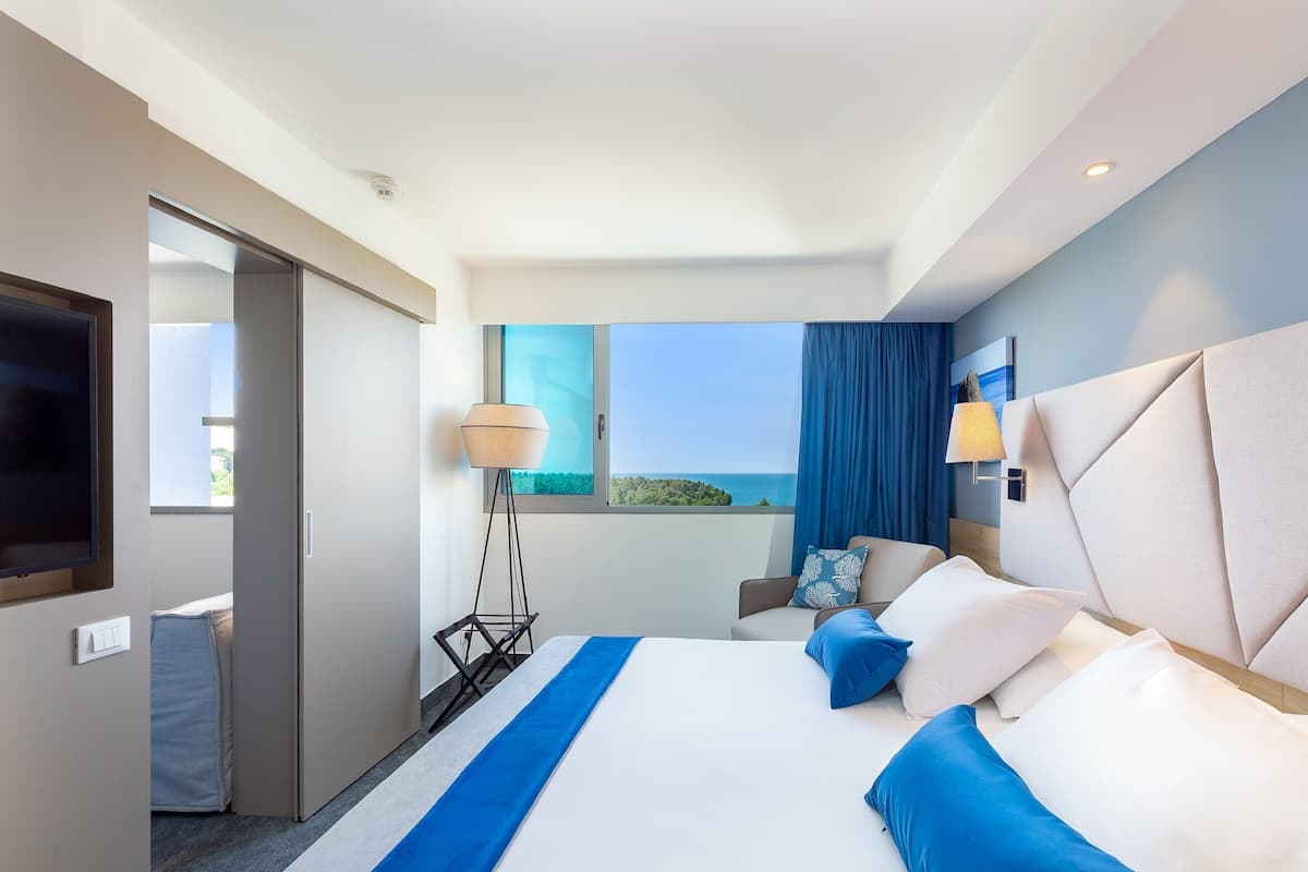 Un hotel moderno con una cama grande, televisión, escritorio y vista al mar.