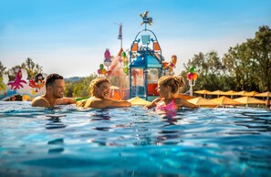 A swimming pool with a water slide and umbrellas in the background.