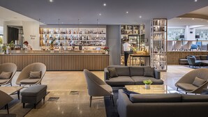 A modern bar area with a variety of liquor bottles, a seating area with sofas and armchairs, and a large window providing a view of the outdoors. - Valamar Diamant Hotel (Porec)