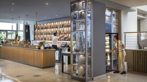 A modern bar area with a wooden reception desk, a glass display case with bottles, and a refrigerated section with glasses. - Valamar Diamant Hotel (Porec)