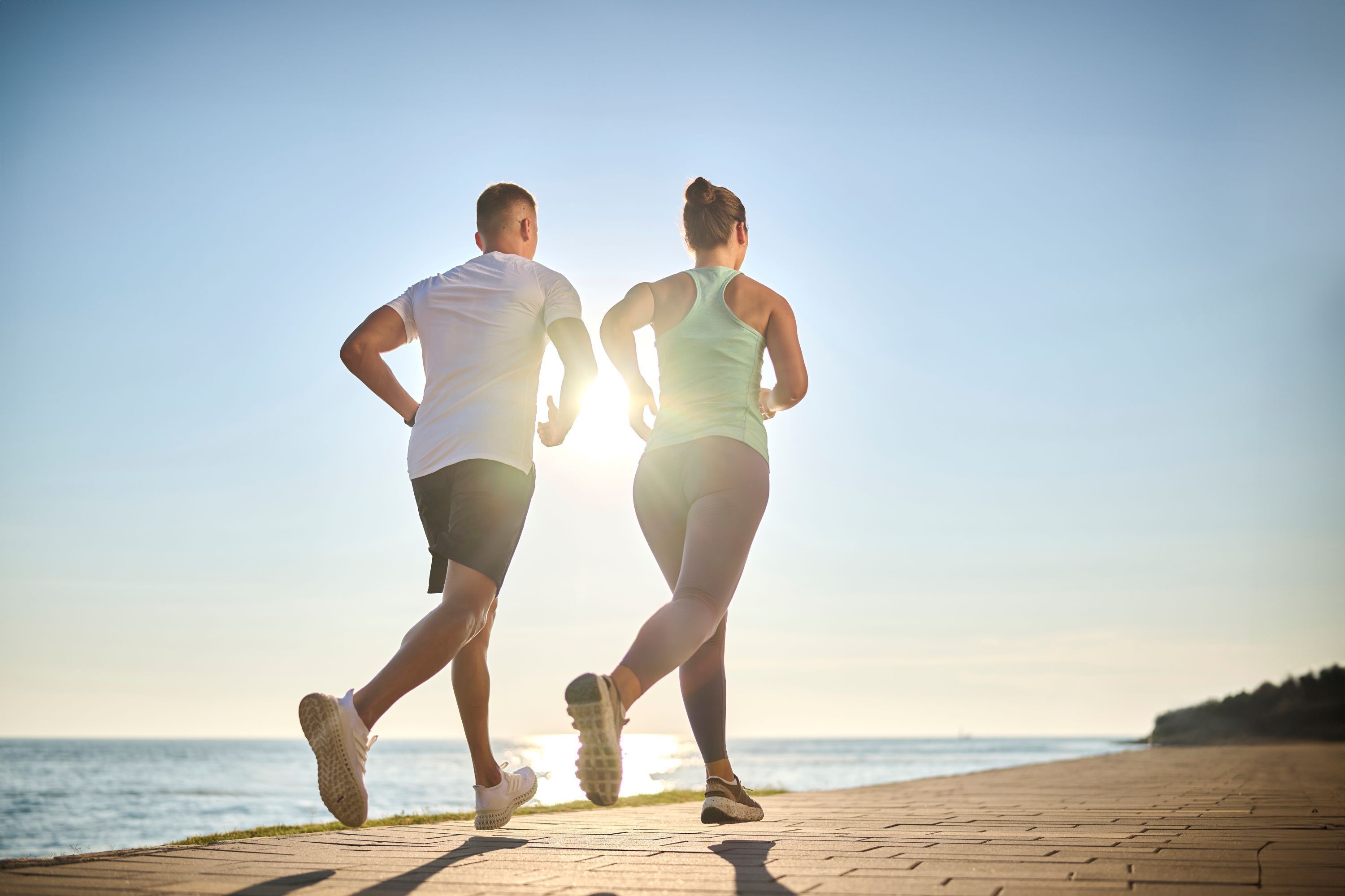 Two people jogging on a paved path by the sea during sunset.