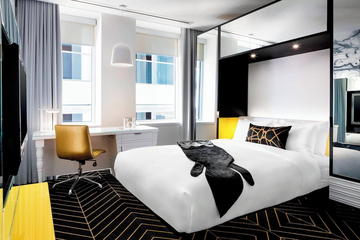 A modern hotel room with a large bed, a desk, and a chair.