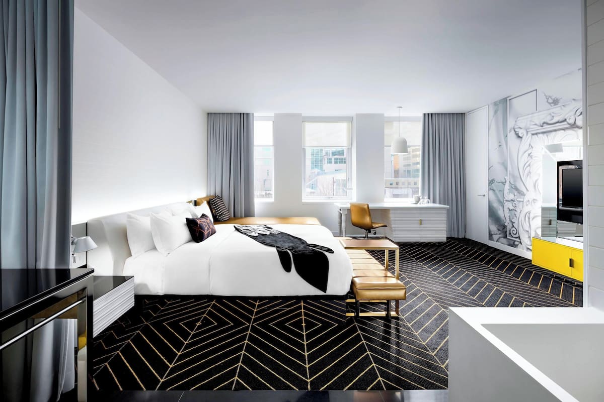 A modern hotel room with a large bed, a desk, and a view of the city.