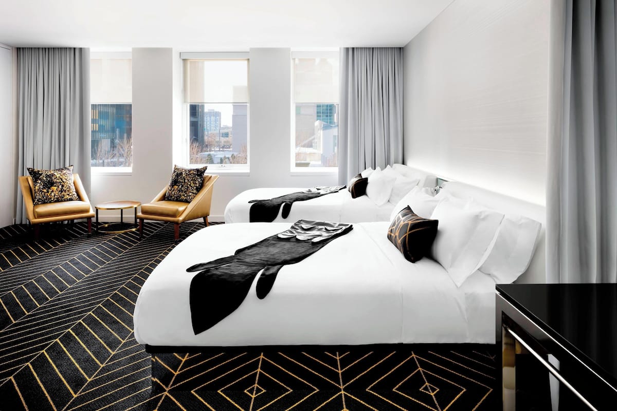 A hotel room with two beds, a large window, a city view, and a modern design.