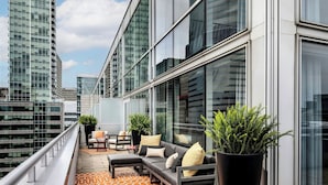 Uma área de estar moderna ao ar livre, com um sofá, cadeiras e plantas em vasos, com vista para um horizonte urbano.