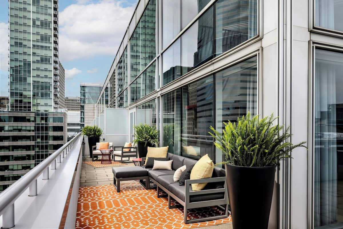 A modern outdoor seating area with a sofa, chairs, and potted plants, overlooking a cityscape.