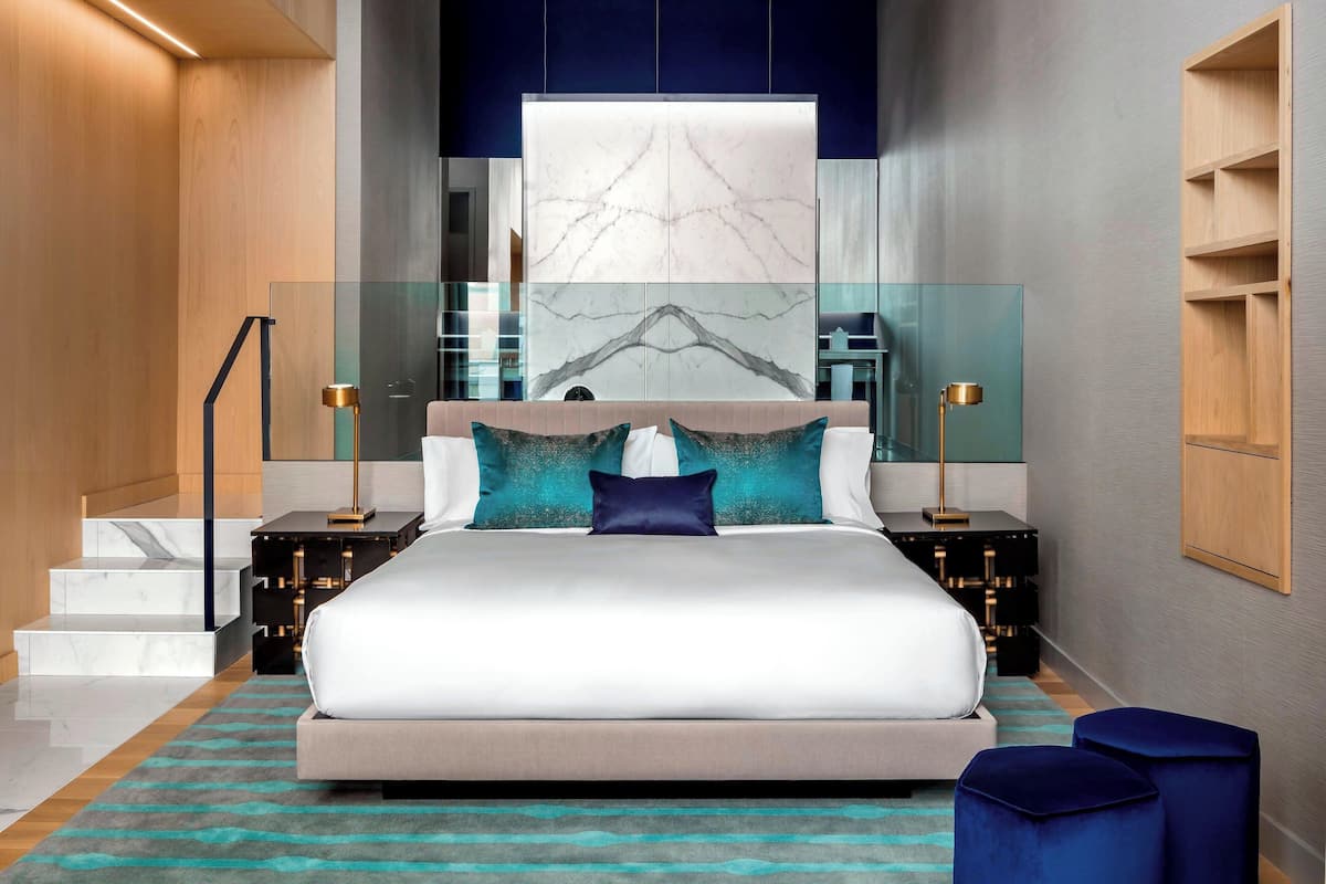 A modern bedroom with a large bed, glass panels, and a marble wall.