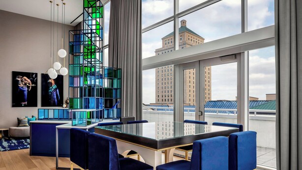 Uma sala de jantar moderna com mesa de vidro, cadeiras estofadas em azul e vista para a cidade.