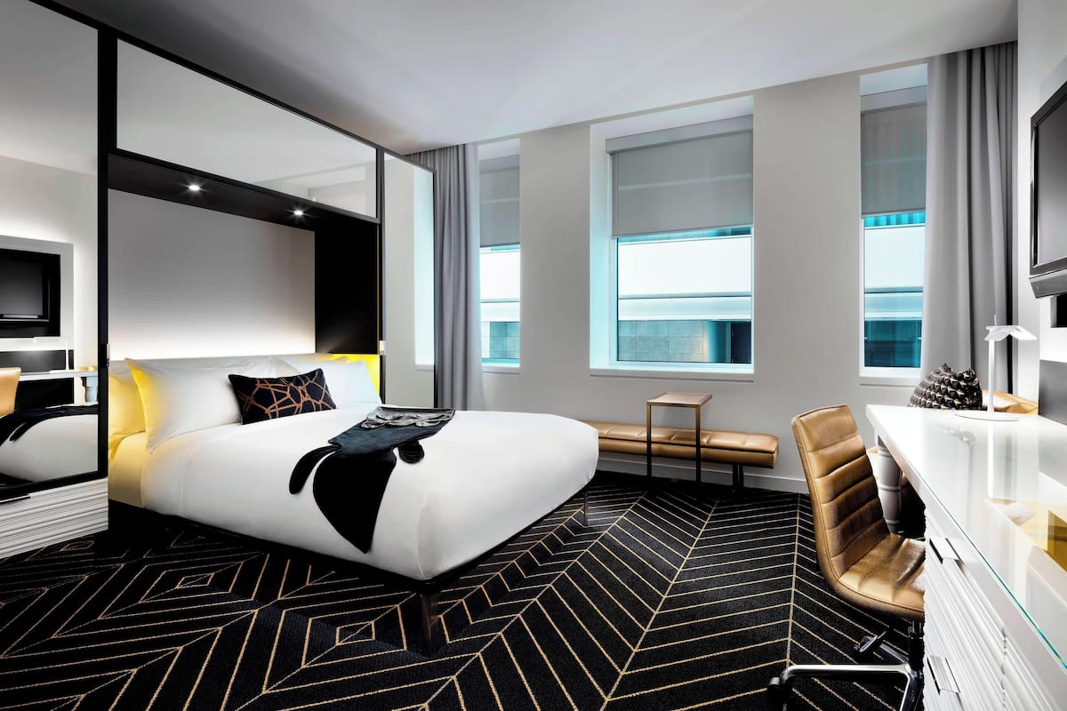 A modern hotel room with a large bed, a desk, a chair, and a view of the city.
