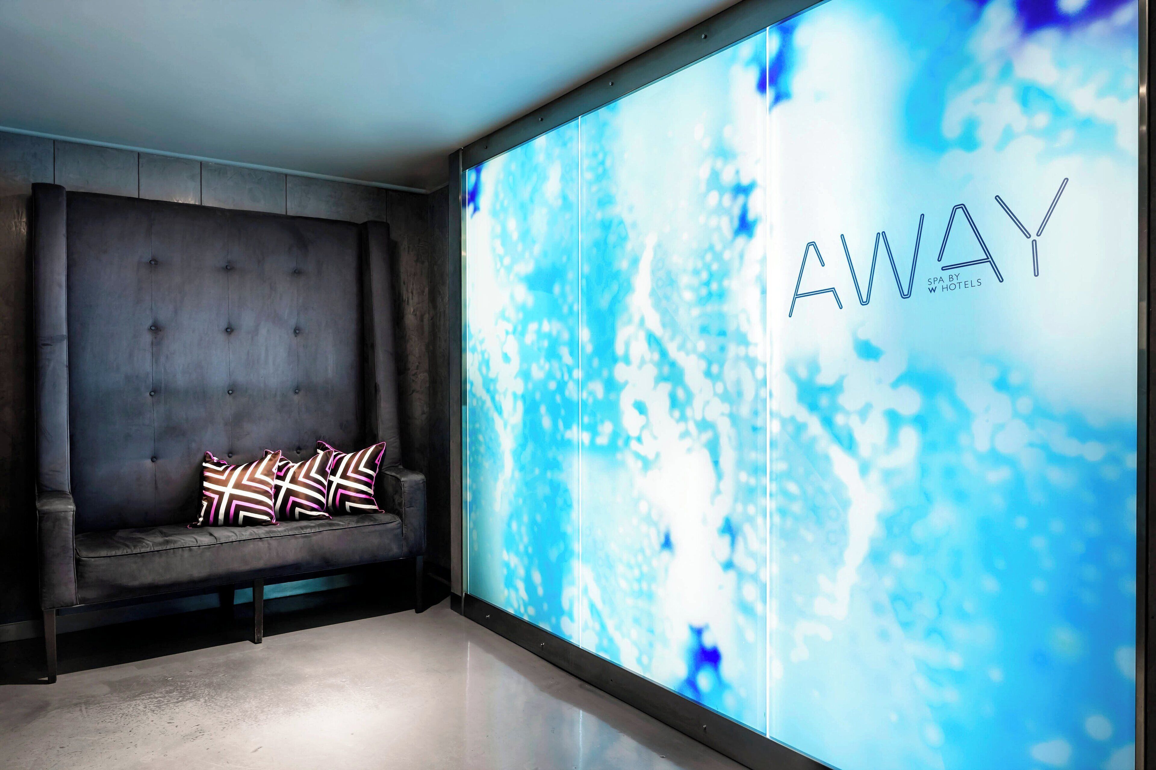 Um lobby moderno com um sofá em tons escuros e uma grande tela digital exibindo a palavra "AWAY".