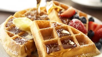 Ein Teller Waffeln mit Sirup, Butter und Früchten.