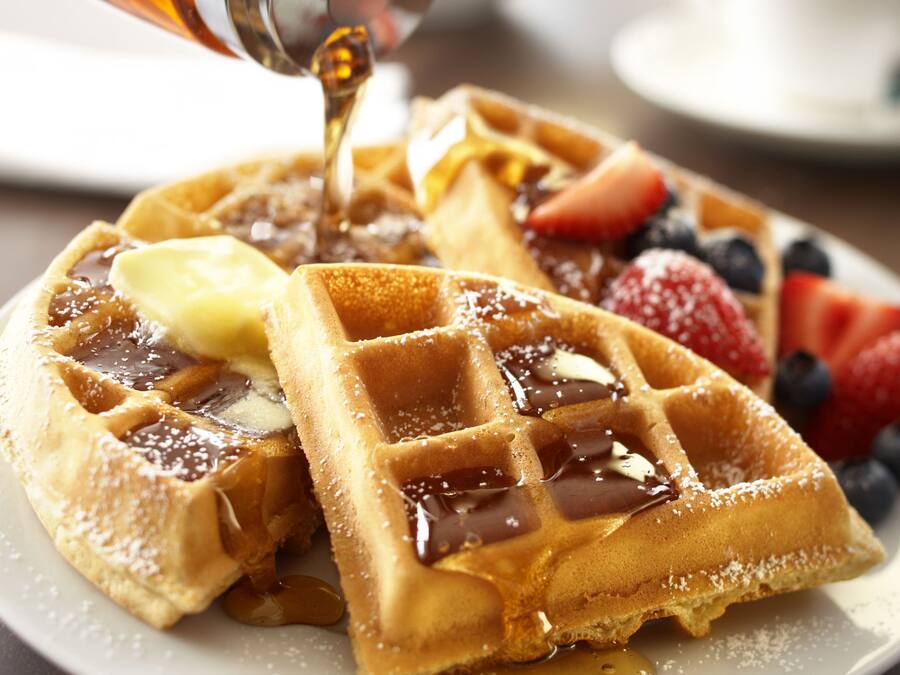 Ein Teller Waffeln mit Sirup, Butter und Früchten.