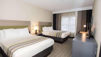 A hotel room with two beds, a desk, a lamp, and a large window with curtains.