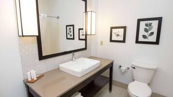 A modern bathroom with a large mirror, white sink, and toilet. There are framed botanical prints on the wall.