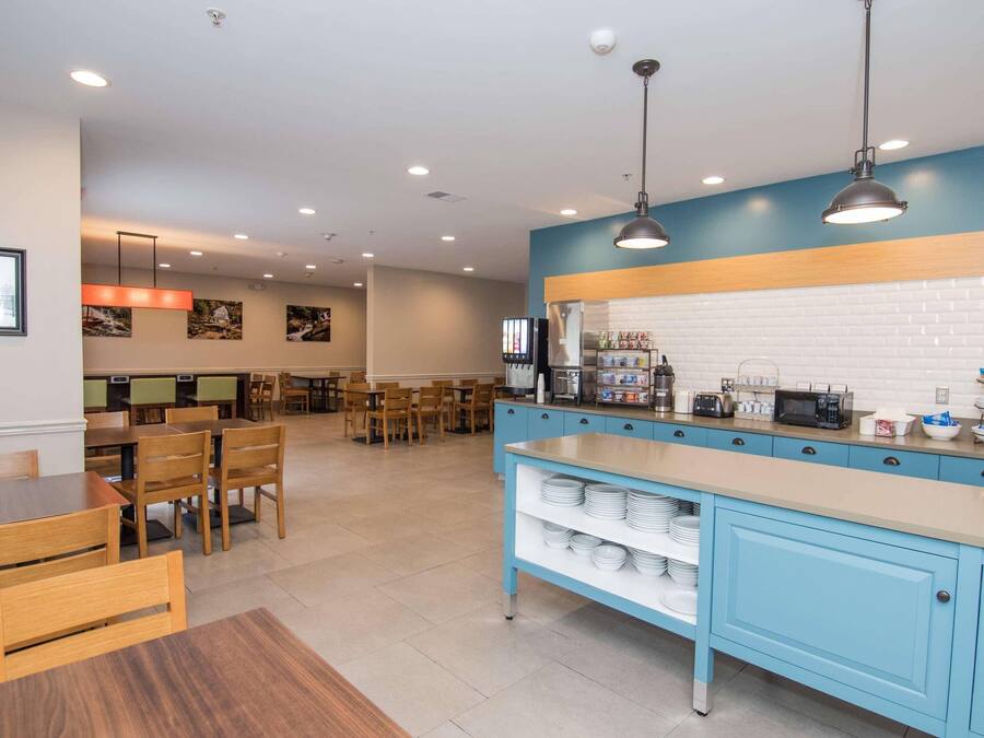 A modern cafe with a long counter, seating area, and a kitchen with appliances.