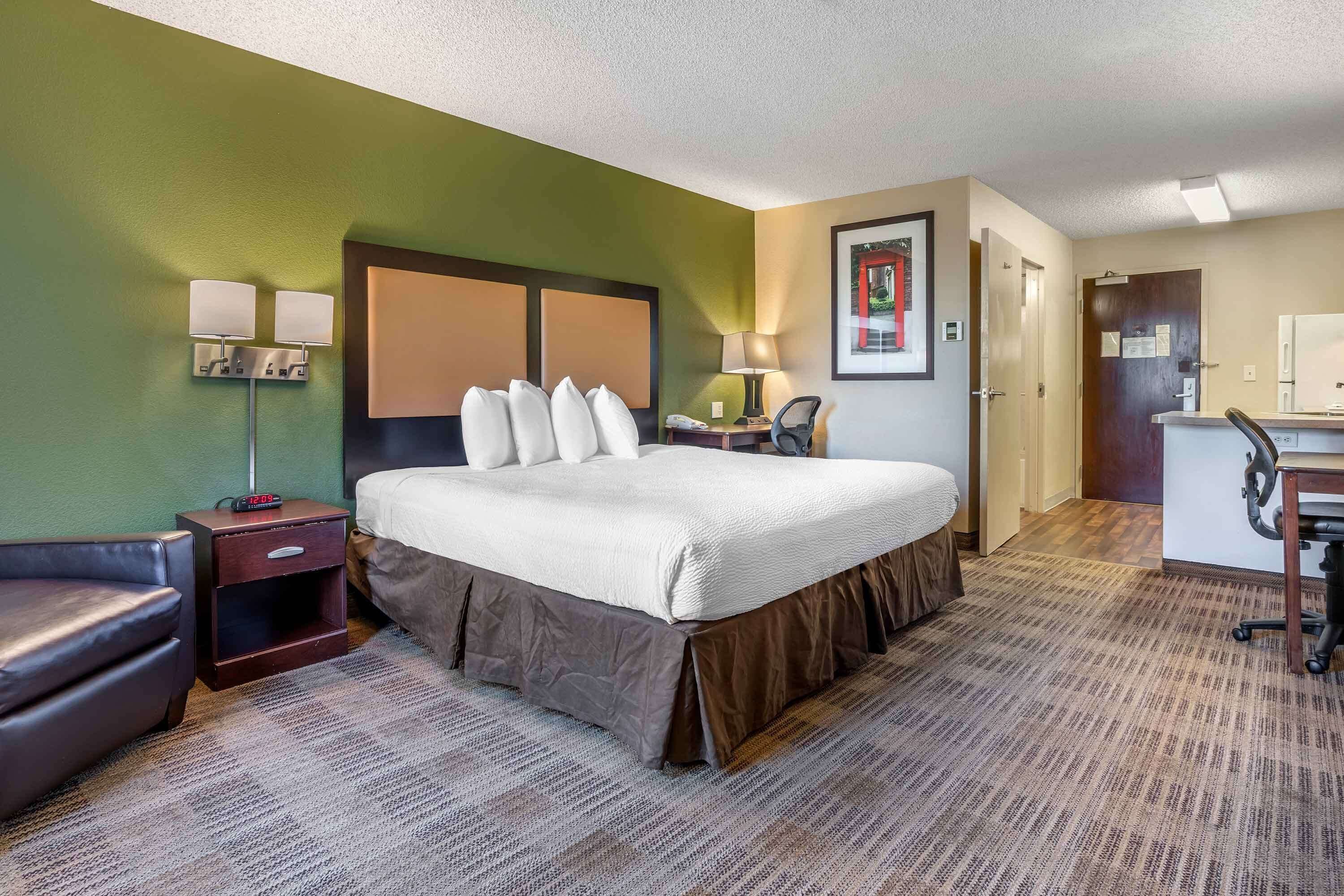 A hotel room with a large bed, a desk, a chair, a nightstand, and a lamp.