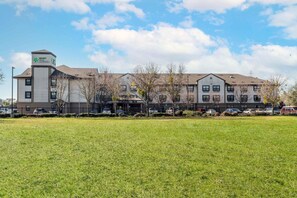 A Stay America hotel with a parking lot and a grassy field in the foreground. - Extended Stay America Suites Sacramento West Sacramento (West Sacramento)