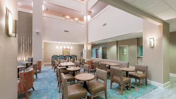 A hotel lobby with multiple seating areas, including round tables and booths, and a high ceiling with recessed lighting.