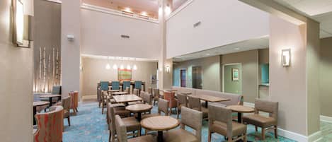 Un hall de hotel con varias zonas de estar, incluyendo mesas redondas y cabinas, y un techo alto con iluminación empotrada.