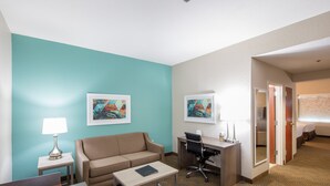 Een hotelkamer met een turquoise accentmuur, een bank, een bureau met stoel, een klein tafeltje en twee ingelijste kunstwerken.