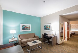 A hotel room with a teal accent wall, a sofa, a desk with a chair, a small table, and two framed artworks. - Holiday Inn & Suites Lake City by IHG (Lake City)