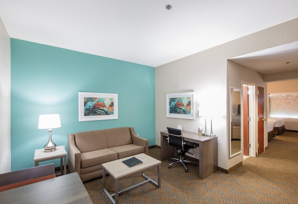 A hotel room with a teal accent wall, a sofa, a desk with a chair, a small table, and two framed artworks. - Holiday Inn & Suites Lake City by IHG (Lake City)