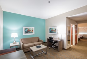 Habitación de hotel con una pared de acento color aguamarina, un sofá, un escritorio con una silla, una mesita y dos cuadros enmarcados.