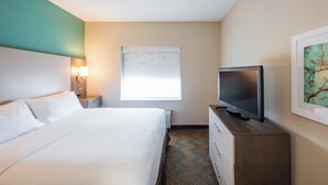 Hotelkamer met een bed, een televisie op een houten dressoir, een nachtkastje met een lamp en een raam met zonwering.