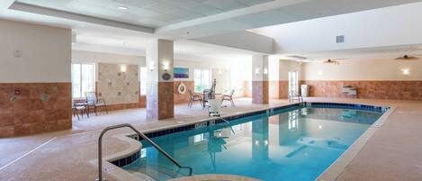 An indoor swimming pool with clear lane markings, a lifeguard chair, and a changing room area.